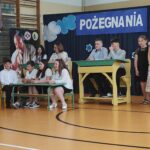 Uczniowie i nauczyciele na uroczystości zakończenia roku szkolnego w będzińskiej szkole. Widoczny baner „Pożegnania Nadszedł”.