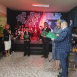 Uroczystość szkolna w Będzinie. Uczniowie i nauczyciele świętują zakończenie roku szkolnego. Widoczny baner „Ocalić od zapomnienia”.