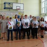 Uczniowie i nauczyciele na uroczystości zakończenia roku szkolnego w Będzinie. Widoczny baner "Wakacje!".