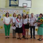 Uczniowie i nauczyciele na uroczystości zakończenia roku szkolnego w Będzinie. Widoczny baner "Wakacje!".