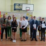 Uczniowie i nauczyciele na uroczystości zakończenia roku szkolnego w szkole w Będzinie. Widoczny baner z napisem "Wakacje!".