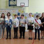 Uczniowie i nauczyciele na uroczystości zakończenia roku szkolnego w szkole w Będzinie. Widoczny baner z napisem "Wakacje!".
