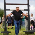 Zawodnik strongman podczas Dożynek Gminnych Tymień 2025 wykonujący chód po jarzmie.