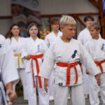 Uczniowie karate w białych gisach i pomarańczowych pasach w Dożynkach Gminne Tymień.