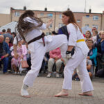 Dwie kobiety na sparingu karate podczas Dożynek Gminnych Tymień. Jeden wykonuje wysokie kopnięcie.