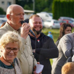 Mężczyzna przemawia do mikrofonu w Dożynkach Gminnych Tymień 2025. Uważna publiczność słucha.