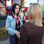 Kobieta odbiera nagrodę w Dożynkach Gminnych Tymień 2025. Ma na sobie dżinsową kurtkę i medal.