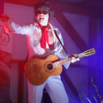 Odtwórca Elvisa Presleya występuje w Dożynkach Gminnych Tymień 2025 grając na gitarze.