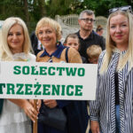 Kobiety w Dożynkach Gminne Tymień 2025 trzymające tabliczkę z napisem „Sołectwo Strzeżenice.