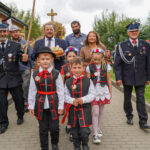 Procesja Dożynek Gminnych Tymień 2025: dzieci w tradycyjnych strojach polskich oraz dorośli niosący chleb i krzyż dożynkowy.