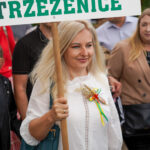 Kobieta w Dożynkach Gminne Tymień 2025, trzymająca tabliczkę z napisem „Sołectwo Trzeżenice.