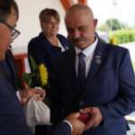 Mężczyzna odbiera nagrodę na Dożynkach Gminnych Tymień 2025. Wręczono mu małe pudełko i słonecznik.
