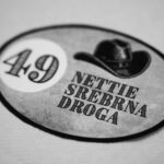 Odznaka z napisem „49 Nettie Srebrna Droga” i kowbojskim kapeluszem, nawiązująca do osób starszych na Dzikim Zachodzie.