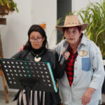 Dwie kobiety w kowbojskich strojach na imprezie Seniorzy na Dzikim Zachodzie, jedna trzyma mikrofon.